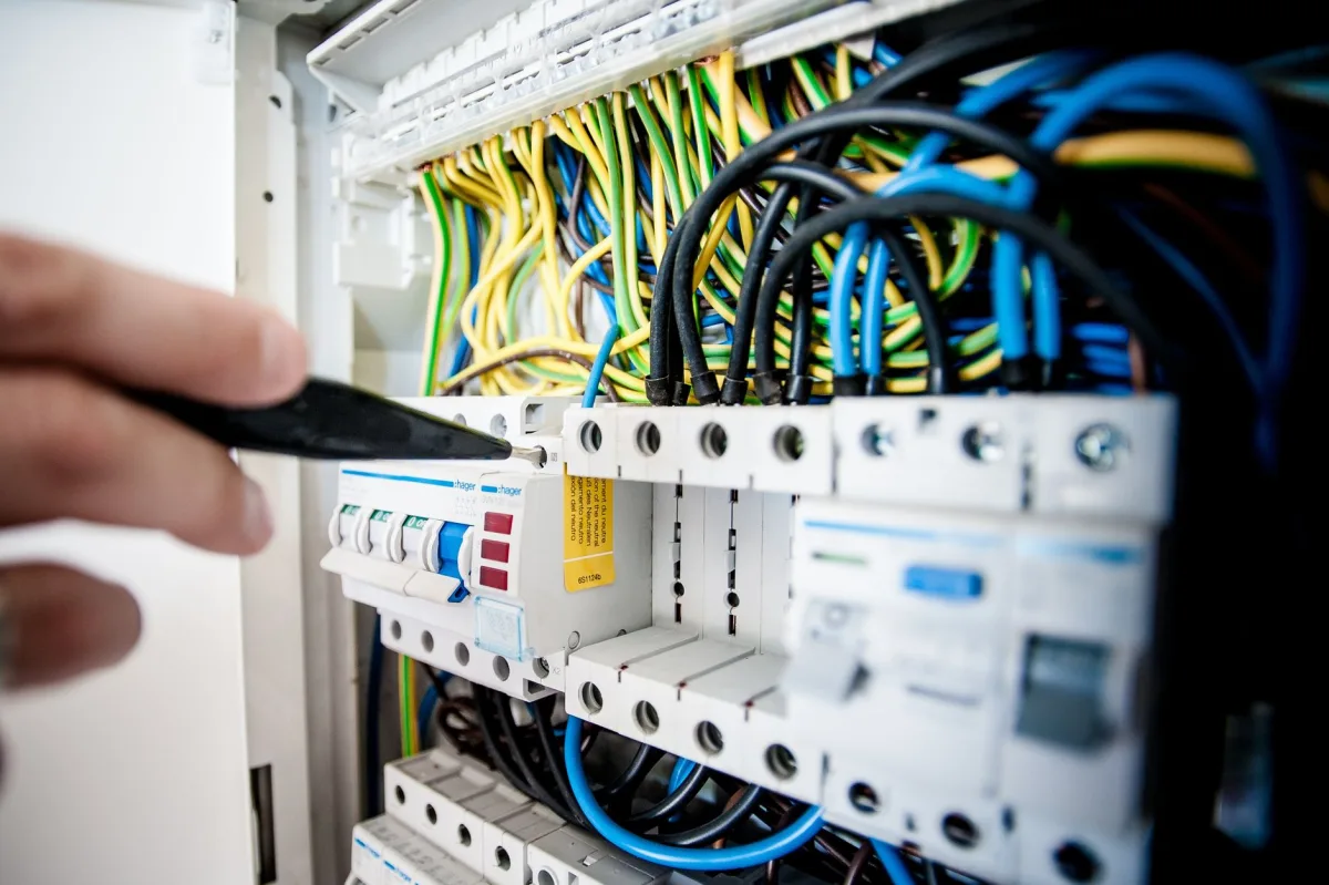 Hand of electrician working on a circuit breaker with colorful wires, ensuring safe connections. Hand of electrician working on a circuit breaker with colorful wires, ensuring safe connections.